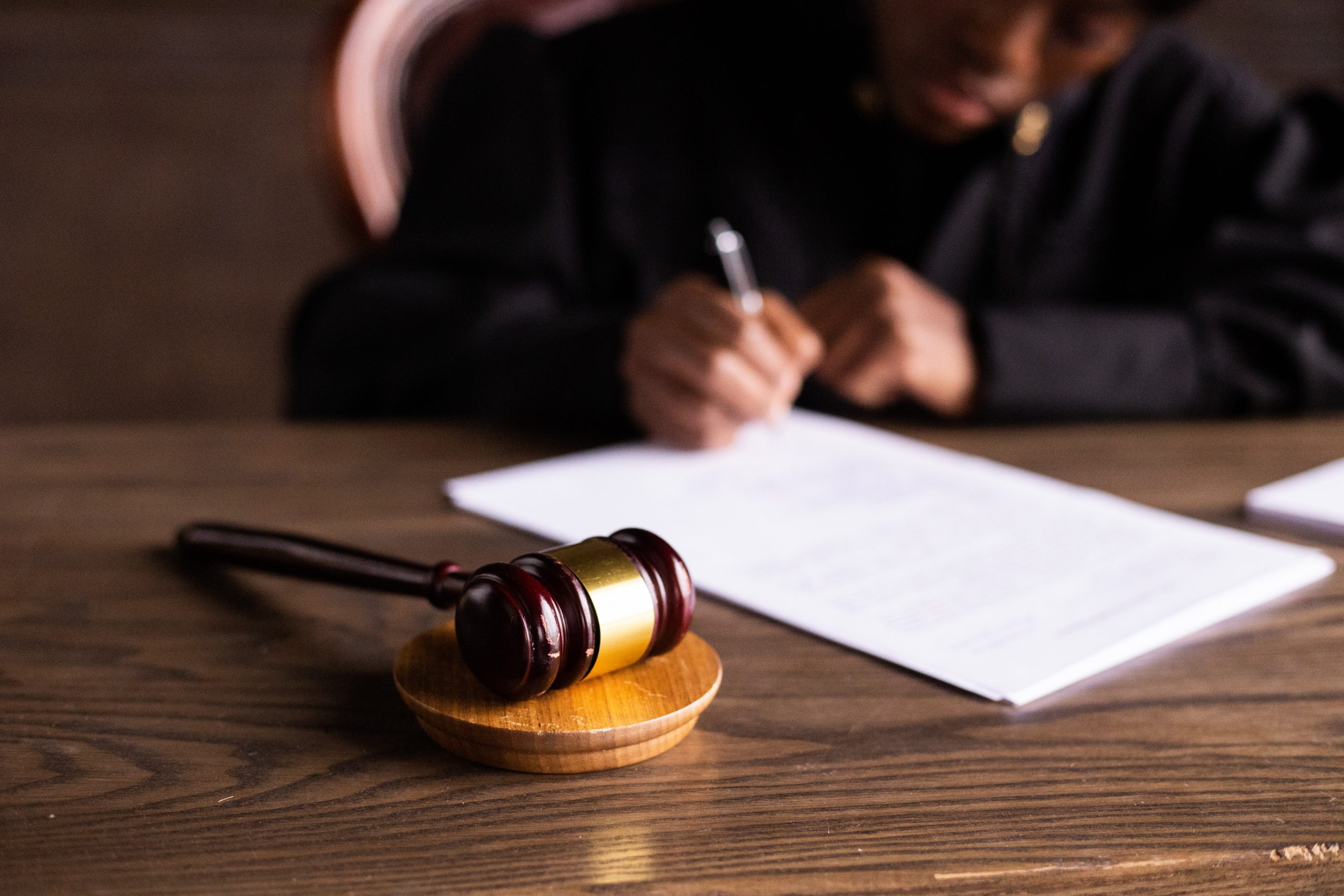 Close-up of a Gavel with a Judge Signing a Document Behind It-1